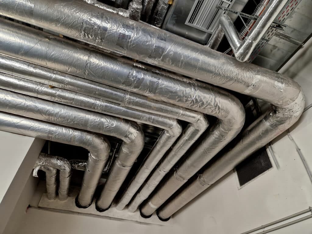 Silver metallic pipes with insulation, arranged in a pattern on a ceiling