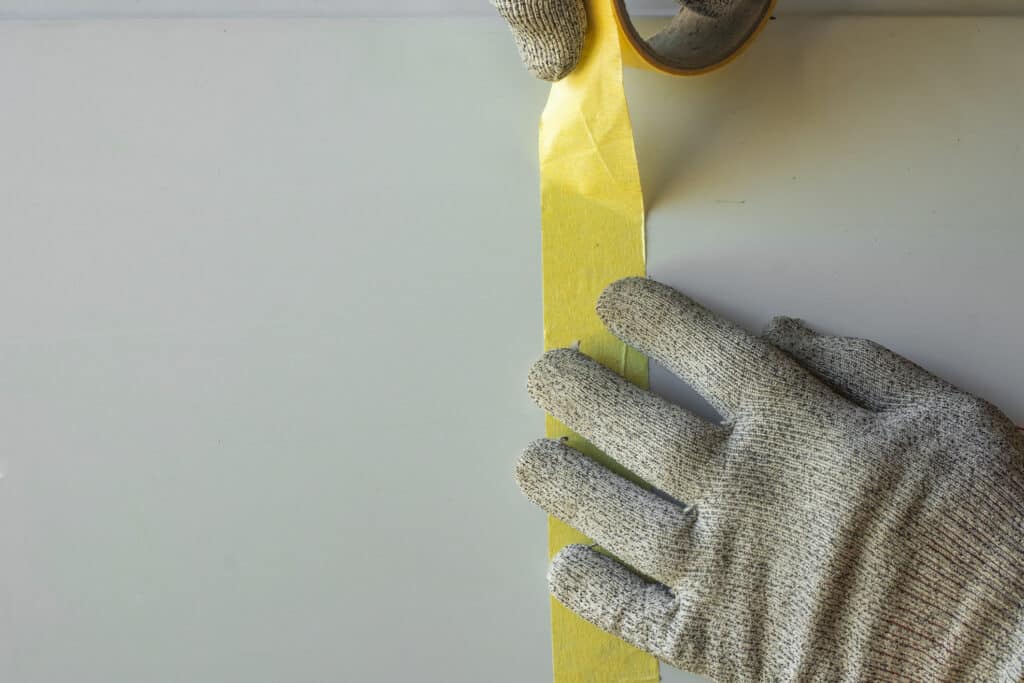 A worker glues masking tape to a car door.