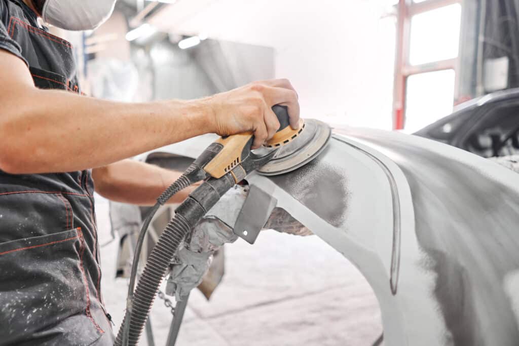 Mechanic using grinding tool to sand car elements down.