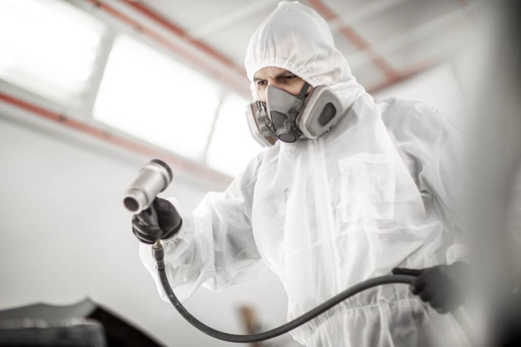 Mechanic in full PPE spraying a car