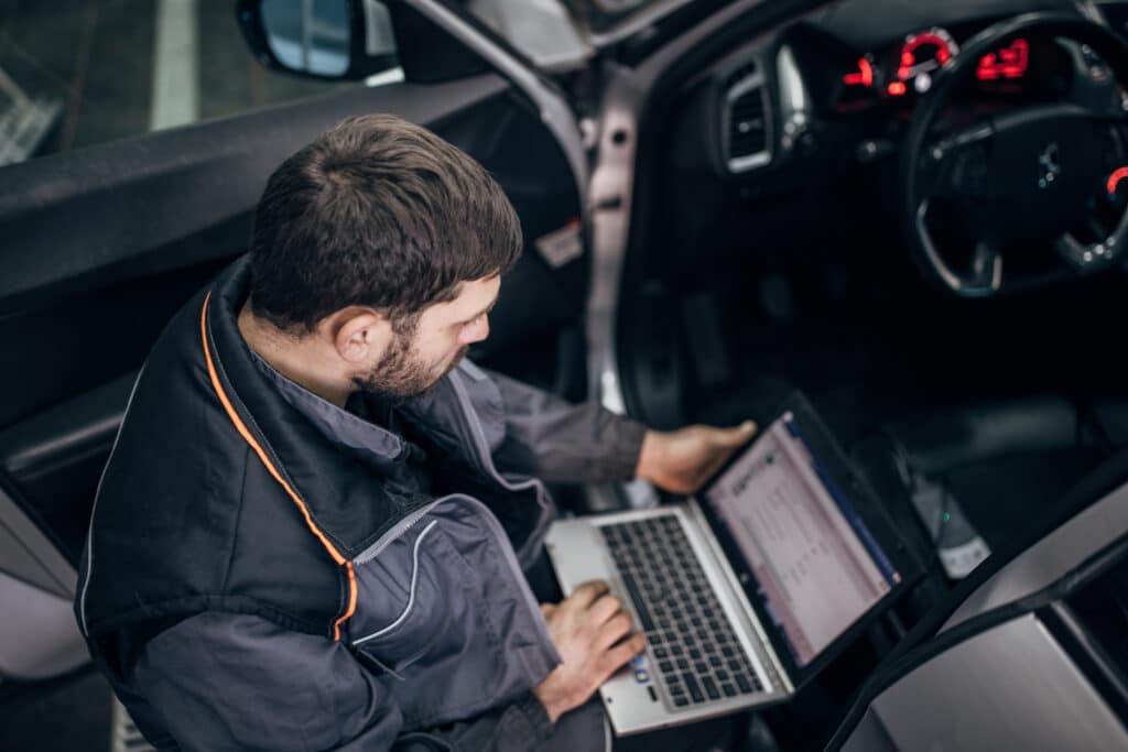 Male mechanic looking at a laptop and analysing data on a car