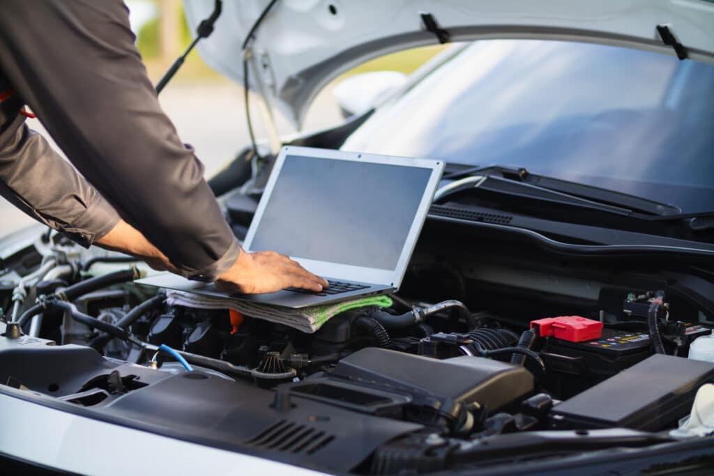 Mechanic using laptop whilst looking into a car engine